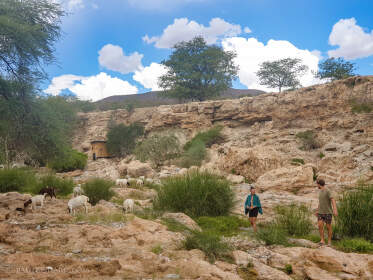 James & Naomi walking along river near goats & sheeps at campsite