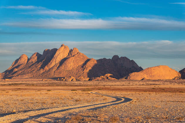 track through rocky plain with dry grass & red hills at sunset