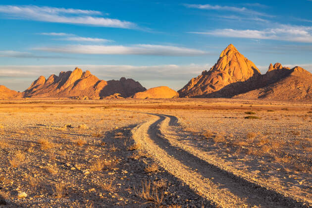 track through rocky plain with dry grass & red hills at sunset