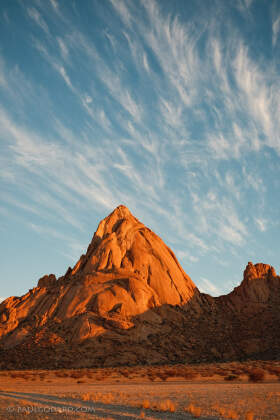 rocky plain with dry grass & red hills at sunset