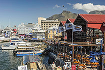 boats in waterfront harbour + restaurants in old buildings + table mt + clouds