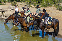 people & guide (West) riding horses at water hole