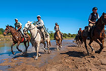 people on horses cantering in river