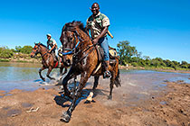 people on horses cantering in river