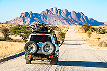 land cruiser on road through desert plain & moutains at sunset