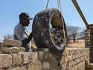 workers filling cement around glass bottles in tyre while building workshop wall