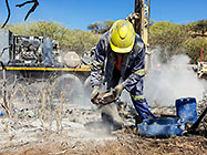 Human worker sampling gravel from borehole drilled  in riverbed