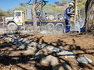 Human worker sampling gravel from borehole drilled  in riverbed