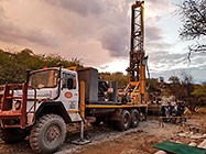 Human truck & workers drilling borehole in riverbed at sunset