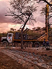 Human truck & workers drilling borehole in riverbed at sunset