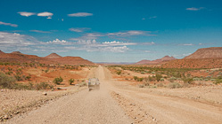 ranger camper in dust on gravel road & hills under clouds