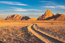 track through rocky plain with dry grass & red hills at sunset