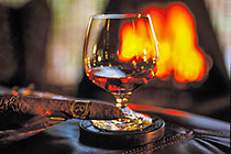 glass of cognac & Cuban cigar on leather table in front of fire